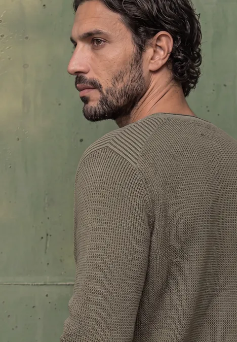 Ein Mann in grünem Strickpullover, Seitenprofil vor grünem Hintergrund.