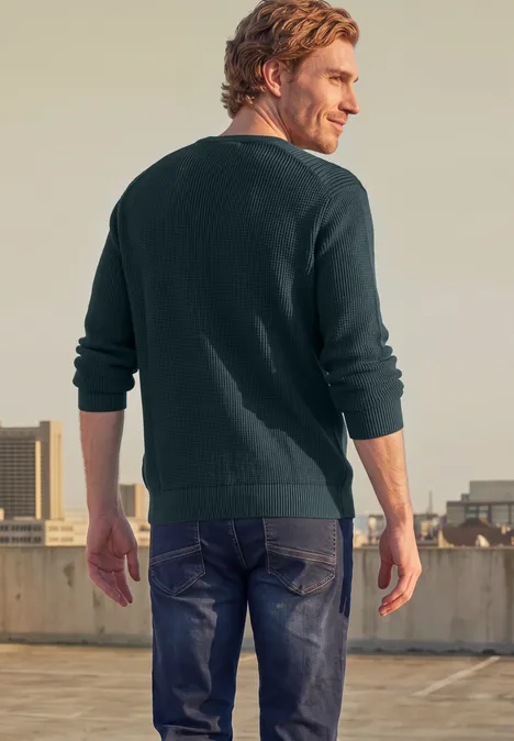 Trui in tweekleurige uitvoering met ronde hals dark fjord blue Ein Mann in grünem Pullover und Jeans steht mit dem Rücken zur Kamera auf einem Dach.