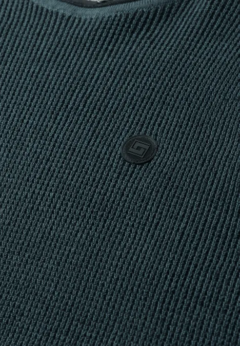 Trui in tweekleurige uitvoering met ronde hals dark fjord blue Nahaufnahme eines dunkelgrauen Strickpullovers mit V-Ausschnitt und kleinem Logo-Emblem auf der Brust.