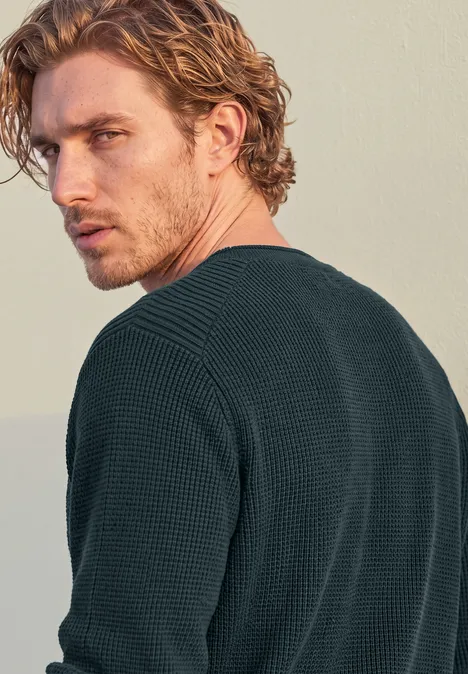 Trui in tweekleurige uitvoering met ronde hals dark fjord blue Ein junger Mann mit lockigem blondem Haar im dunklen Pullover blickt über die Schulter zur Seite.