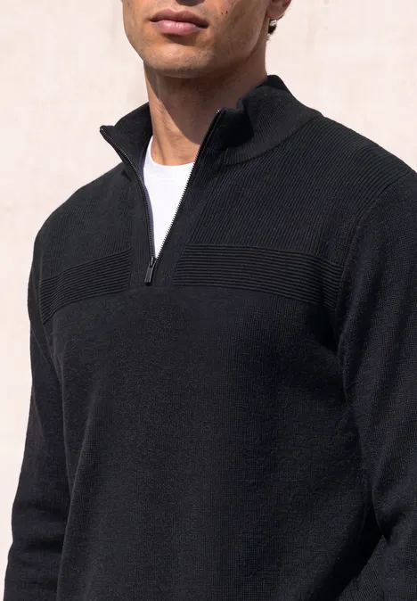 Ein Mann trägt einen schwarzen Pullover mit kurzem Reißverschluss und weißem T-Shirt.