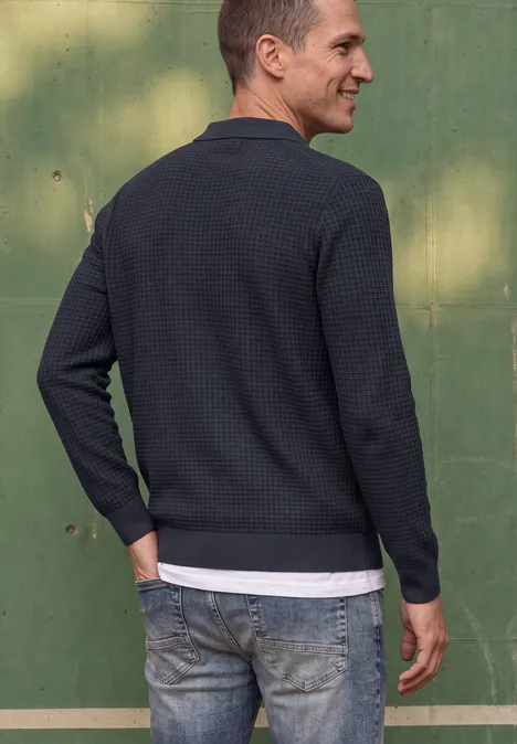 Trui met polokraag en wafelstructuur dark ink blue Ein Mann steht seitlich, trägt dunkelblauen Pullover, Jeans, sieht nach links, grüner Hintergrund.