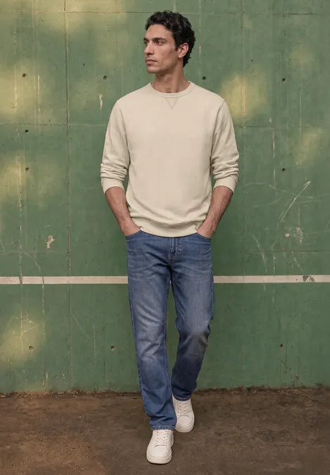 Sweat-shirt en tissu éponge avec détails en tricot côtelé canvas beige Un homme debout devant un mur vert, vêtu d'un haut beige à manches longues, jean bleu et baskets blanches.