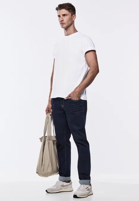 Homme en t-shirt blanc et jean, tenant un sac en tissu beige.
