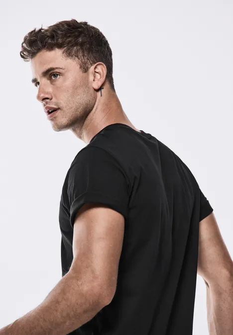 Jeune homme aux cheveux courts en t-shirt noir regarde par-dessus son épaule.