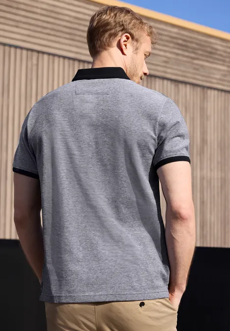 Een man staat met zijn rug naar de camera en draagt een grijs poloshirt met zwarte kraag en mouwboorden.