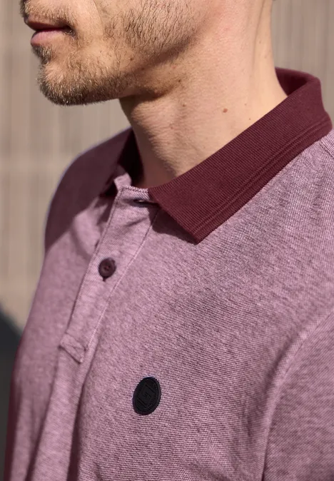 Close-up van een man in lichtpaars poloshirt met donkere kraag en klein zwart logo.