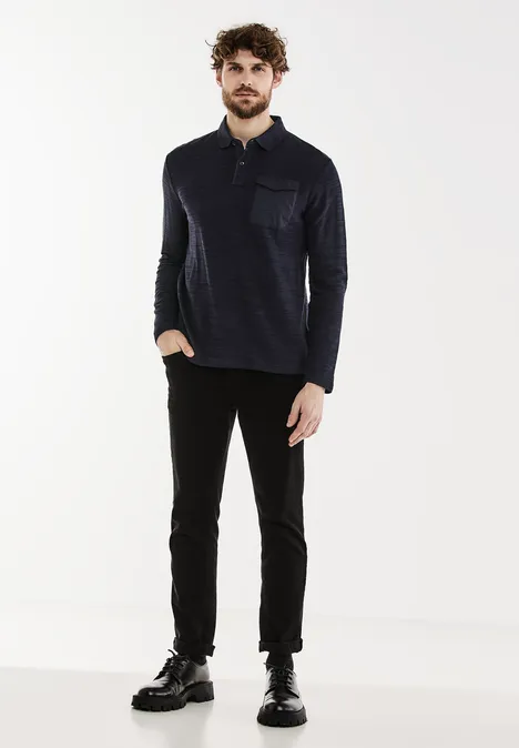 Homme en chemise sombre et pantalon noir sur fond blanc.