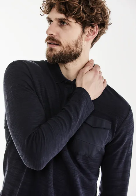 Homme barbu en chemise foncée regarde vers la gauche.