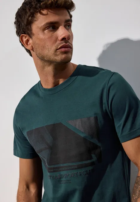 Mann im grünen T-Shirt mit Aufdruck blickt nach links.