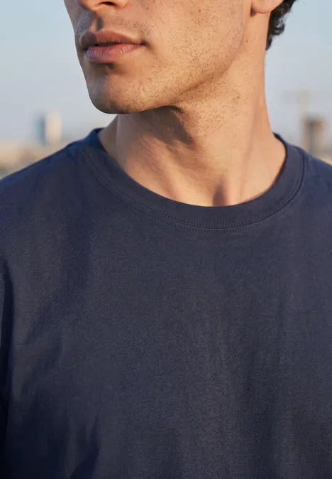 Gros plan d’un homme en t-shirt bleu marine, seuls le cou, le menton et le haut du torse sont visibles.