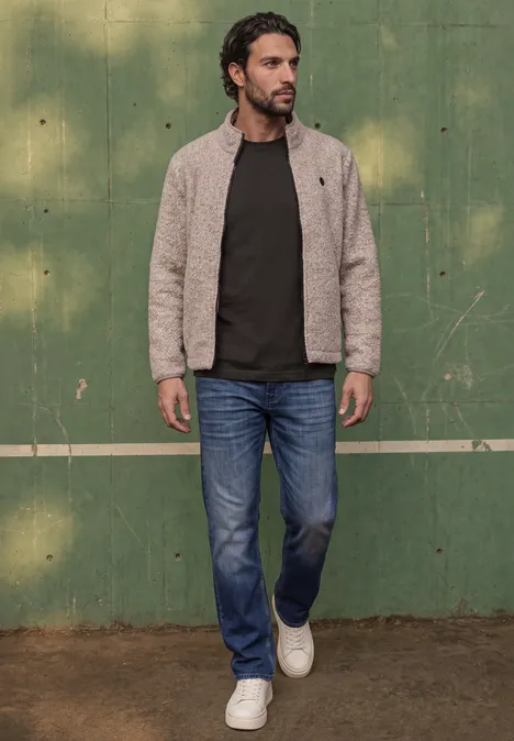 Basic Shirt van puur katoen shadow brown Een man in spijkerbroek, donkergroene trui en beige jas loopt voor een groene muur.
