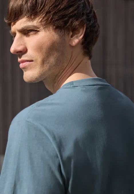 Een man staat met zijn rug naar de camera en kijkt over zijn schouder, hij draagt een blauw T-shirt.