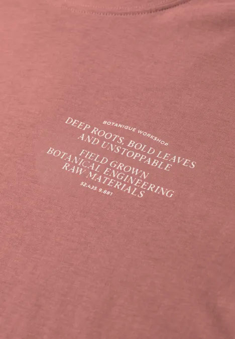Roze T-shirt met witte tekst over diepe wortels, stevige bladeren en duurzame materialen.