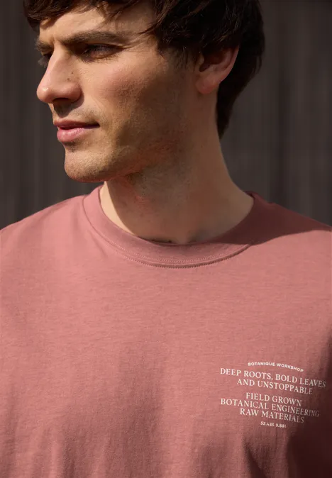 Close-up van een jonge man in een rood t-shirt met witte tekst, zijwaarts kijkend.