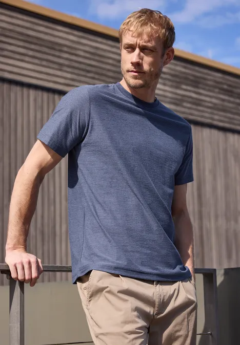 Man leunt op een railing voor een houten wand in een blauw shirt