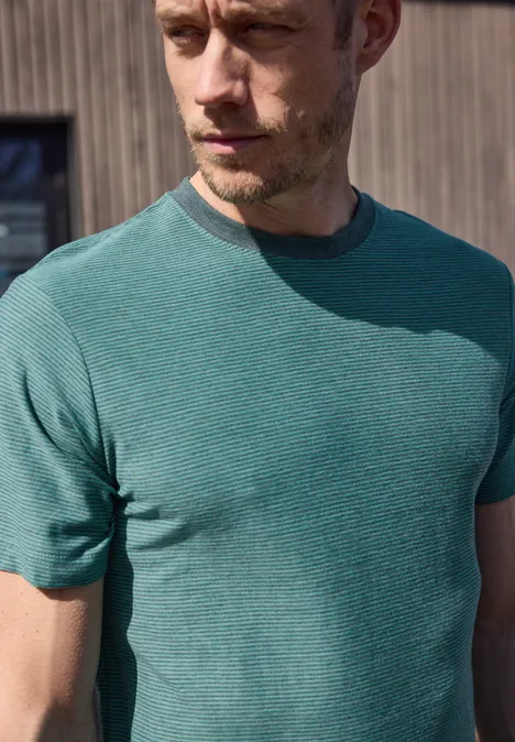 Een vage man in een groen t-shirt voor een houten wand.