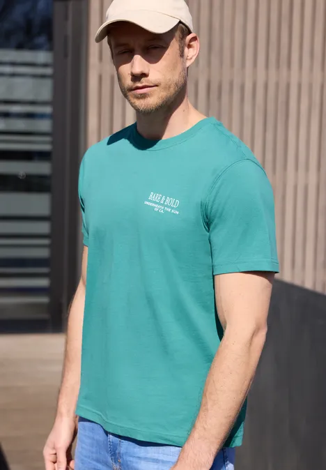 Een man draagt buiten een turkoois T-shirt en een spijkerbroek.