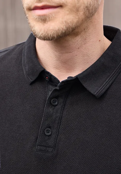 Close-up van het bovenlichaam van een man in een zwart, gestructureerd poloshirt met korte kraag en knopenlijst.