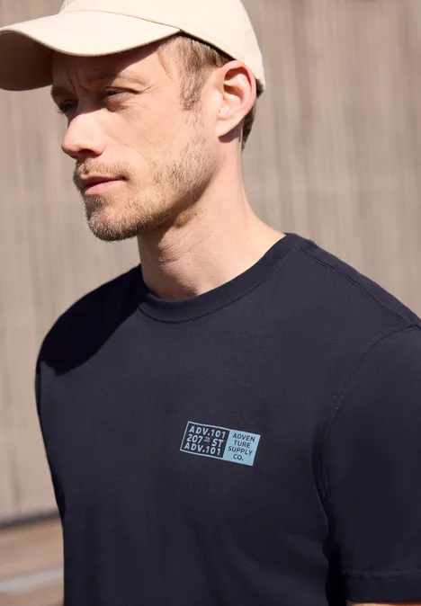 Zijaanzicht van een man in een zwart T-shirt en pet voor een houten wand, gezicht onscherp gemaakt.