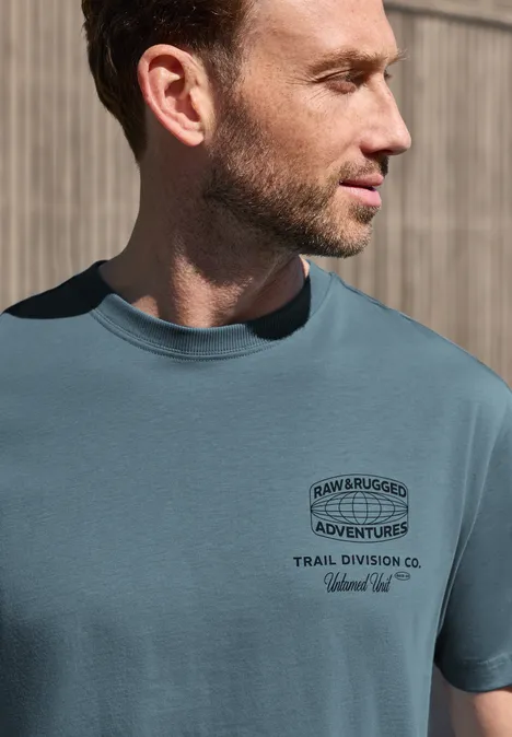Een zijaanzicht van een man met een turkoois t-shirt bedrukt met de tekst 'Adventures'.