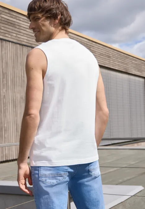 Een man staat met zijn rug naar de camera op een dakterras, draagt een wit hemd en blauwe jeans.