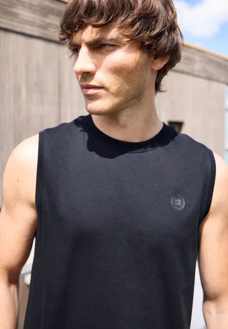 Een atletische man draagt een zwart mouwloos shirt buiten, gezicht onscherp.