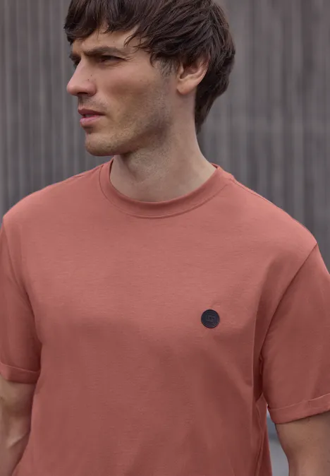 Wazig portret van een persoon in een roestkleurig T-shirt, kijkend opzij voor een grijze muur met verticale latten.