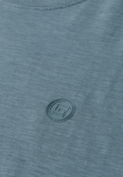 Close-up van een lichtgroen T-shirt met een subtiel, rond logo op de borst.