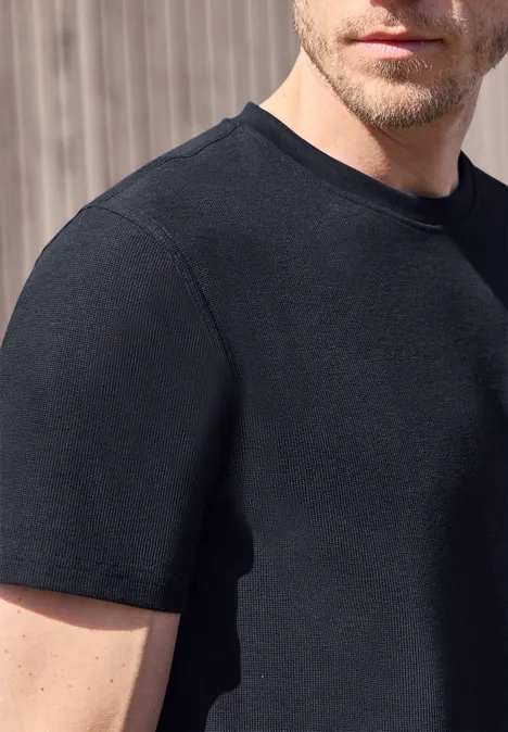 Ein Mann in einem schwarzen T-Shirt vor hellem Hintergrund.