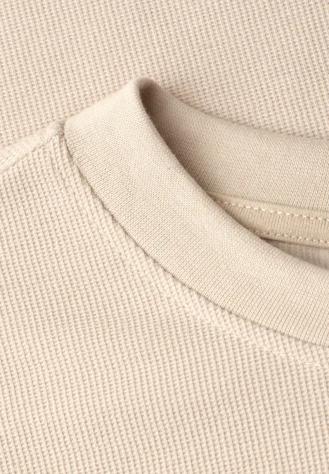 Nahaufnahme eines beigen Rundhalsausschnitts und feinkörnigen Baumwollstrickstoffs.