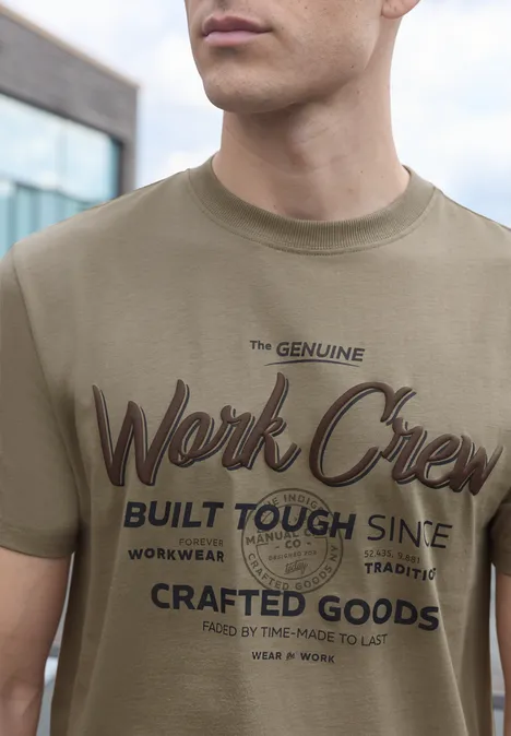 Shirt met ronde hals en Wording Artwork antique beige Man in olijfgroen T-shirt met opdruk „The Genuine Work Crew Built Tough Since… Crafted Goods“.