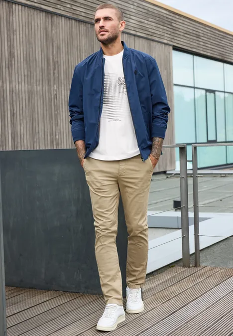 Shirt met ronde hals en opdruk bright white Een man in beige chino, wit t-shirt en blauwe bomberjas loopt over een houten terras.
