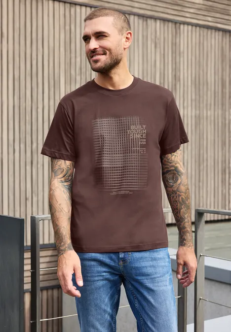 Shirt met ronde hals en print maroon brown Een lachende man in een bruin T-shirt en jeans voor een houten wand, met tatoeages.