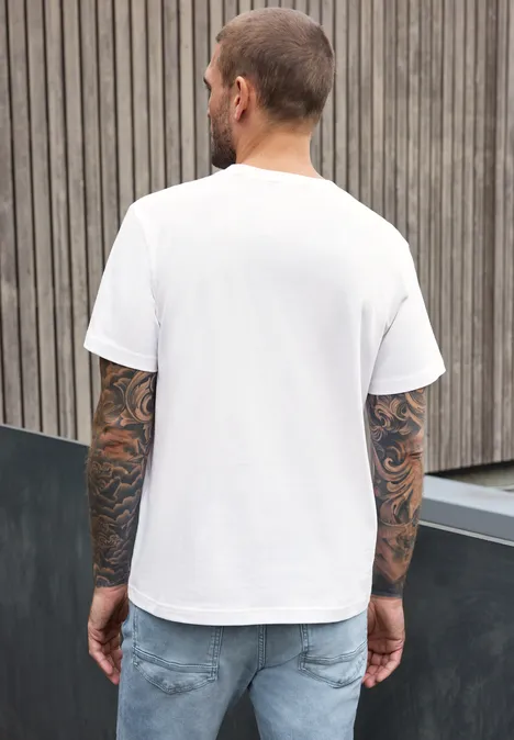 Shirt met ronde hals en opdruk op de borst bright white Een getatoeëerde man in wit t-shirt en spijkerbroek, rugaanzicht voor een houten wand.