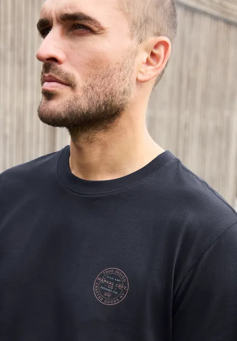 T-Shirt mit Rundhals und Chestprint dark ink blue Ein ernst blickender Mann mit kurzem Haar und dunklem T-Shirt vor Holzplanken.