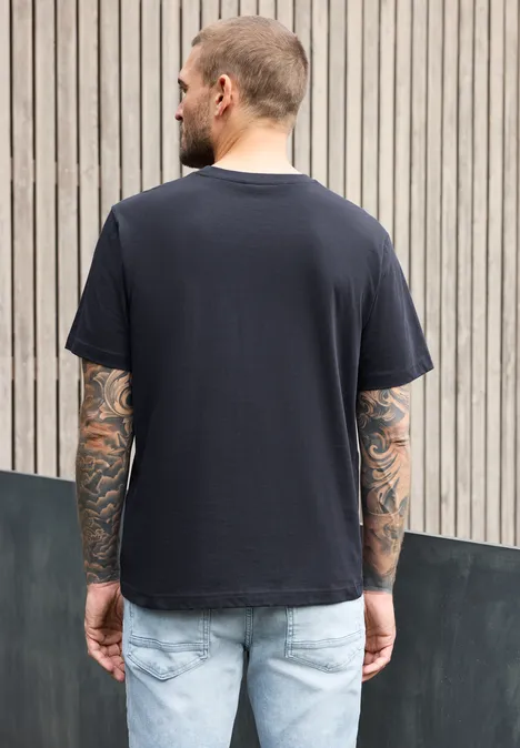T-Shirt mit Rundhals und Chestprint dark ink blue Ein Mann mit Tattoos trägt ein schwarzes T-Shirt und Jeans, steht vor einer Holzlattenwand, Rückenansicht.