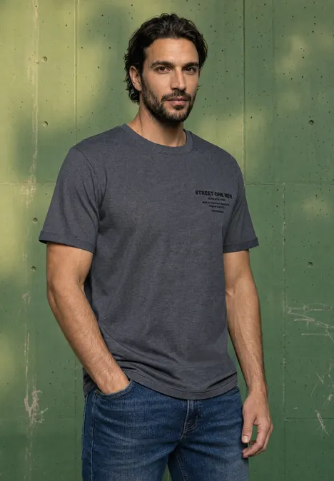 Shirt met ronde hals en opdruk op de borst dark ink blue Een man met donker haar en baard draagt een grijs t-shirt en jeans voor een groene muur.