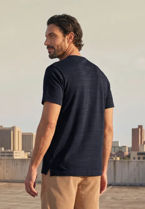 T-Shirt mit Rundhals in Space-Dye-Optik dark ink blue Ein Mann mit dunkelblauer T-Shirt und beige Shorts steht auf einem Dach und blickt über die Stadt.