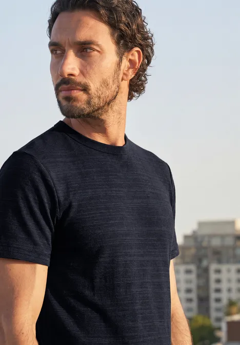 T-Shirt mit Rundhals in Space-Dye-Optik dark ink blue Ein bärtiger Mann mit dunklem T-Shirt blickt seitlich vor urbaner Kulisse.
