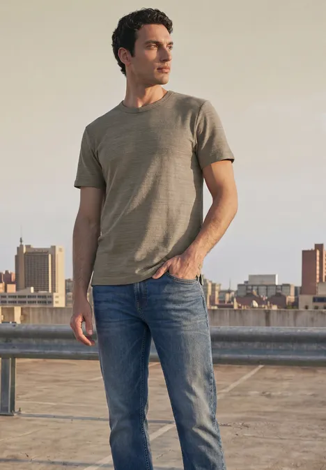 Shirt met ronde hals in space-dye-look antique beige Een man staat op een dak met uitzicht op de stad in een t-shirt en jeans.