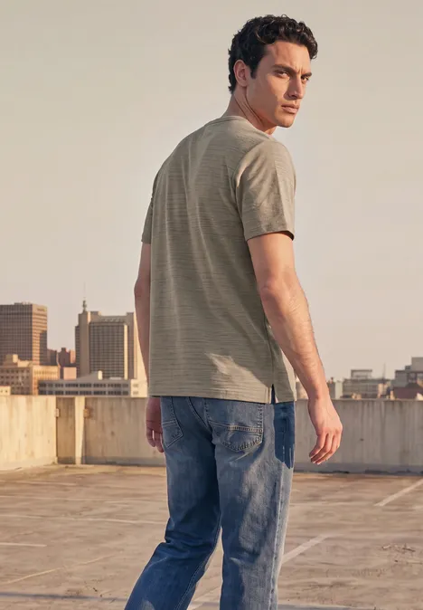 Shirt met ronde hals in space-dye-look antique beige Een man in T-shirt en jeans staat op een dak, met de stad op de achtergrond.
