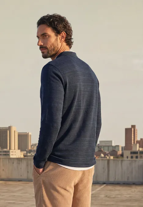 Langarm Poloshirt aus Baumwolle dark ink blue Ein Mann in dunkelblauem Pullover und beigen Hosen steht auf einem Dach und schaut über die Schulter