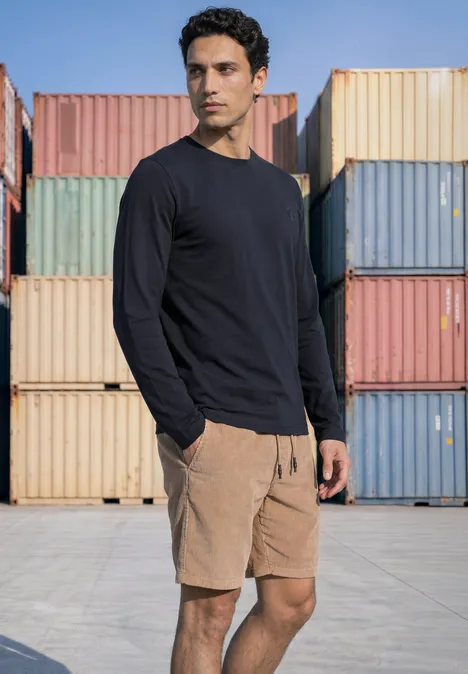 Langarm Shirt mit Rundhals in Unifarbe dark ink blue Ein Mann in schwarzem Shirt und beigen Shorts steht vor bunten Containern.