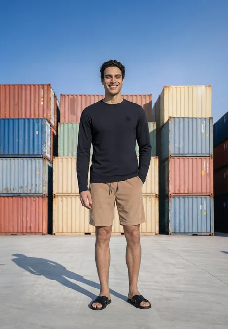 Langarm Shirt mit Rundhals in Unifarbe dark ink blue Ein lächelnder Mann steht vor bunten Frachtcontainern, trägt Langarmshirt, Shorts und Sandalen.