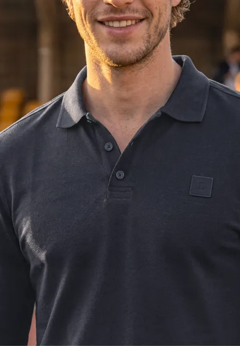 Langarm Poloshirt mit Taschendetail dark ink blue Ein lächelnder Mann trägt ein dunkelgraues Poloshirt vor unscharfem Hintergrund.