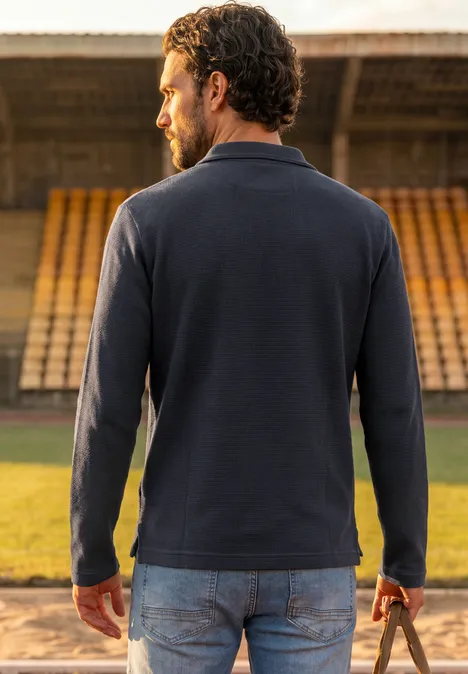 Langarm Poloshirt mit Zipperdetail dark ink blue Ein Mann trägt einen dunklen Pullover und hält einen Ball auf einer Stadiontribüne.