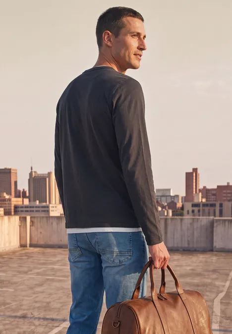 Henleyshirt im 2-in-1-Look dark ink blue Ein Mann im Langarmshirt und Jeans steht auf einem Dach und hält eine Ledertasche, Blick zur Stadt gerichtet.