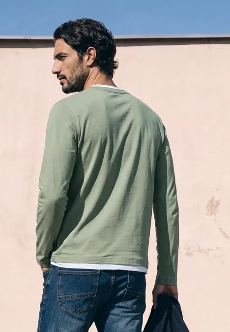 Henleyshirt im 2-in-1-Look willow green Ein Mann steht mit dem Rücken zur Kamera, trägt grünes Langarmshirt und Jeans, hält eine Sonnenbrille.