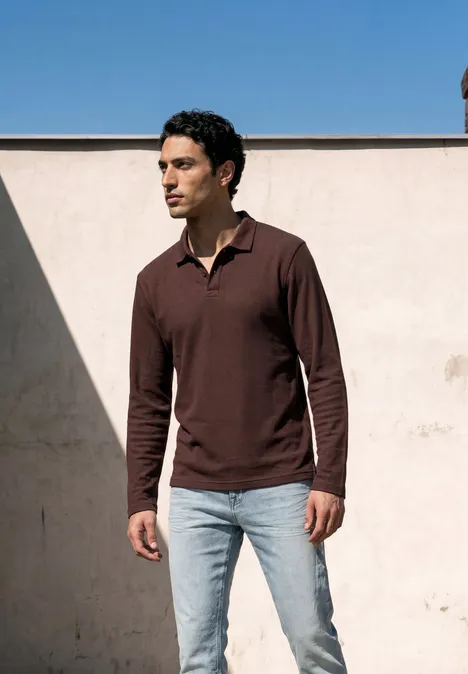Langarm Poloshirt in Unifarbe maroon brown Ein Mann in braunem Langarm-Polo und hellblauen Jeans vor einer hellen Wand